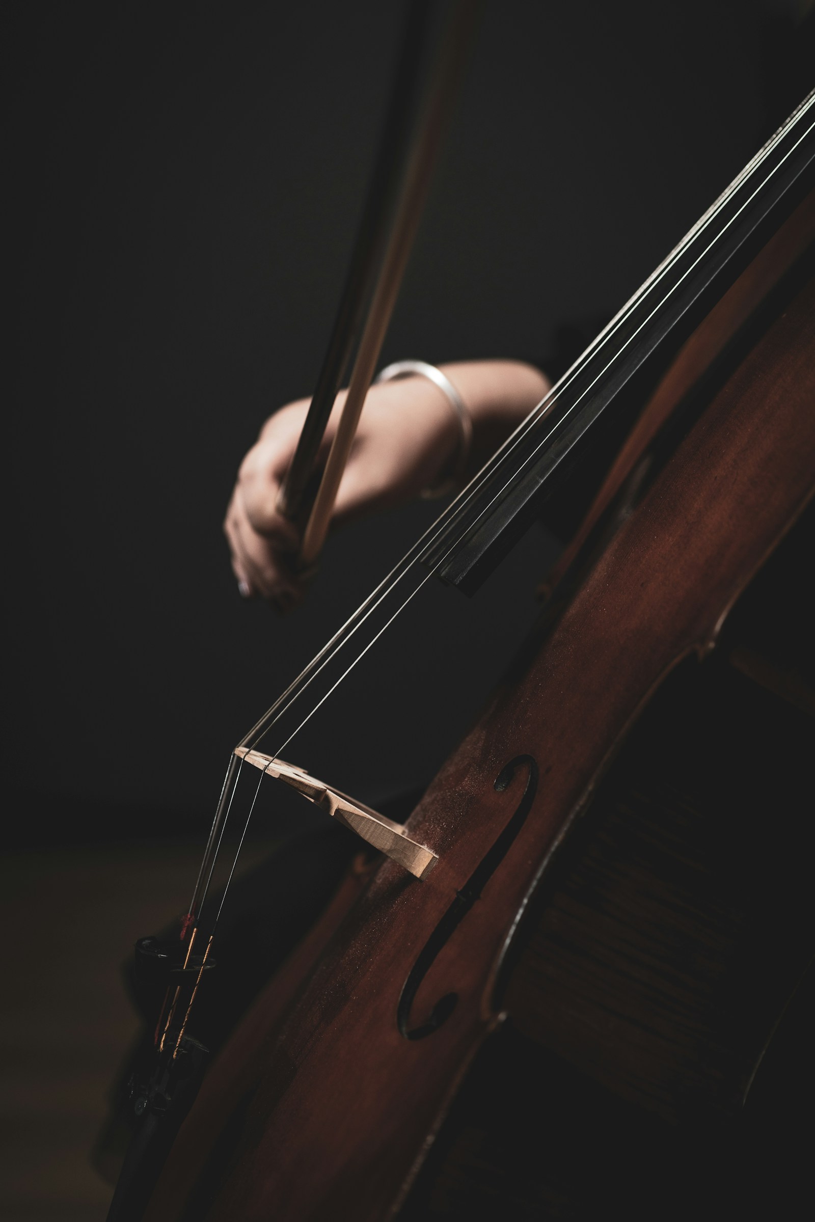 A bow drawing across cello strings, up close