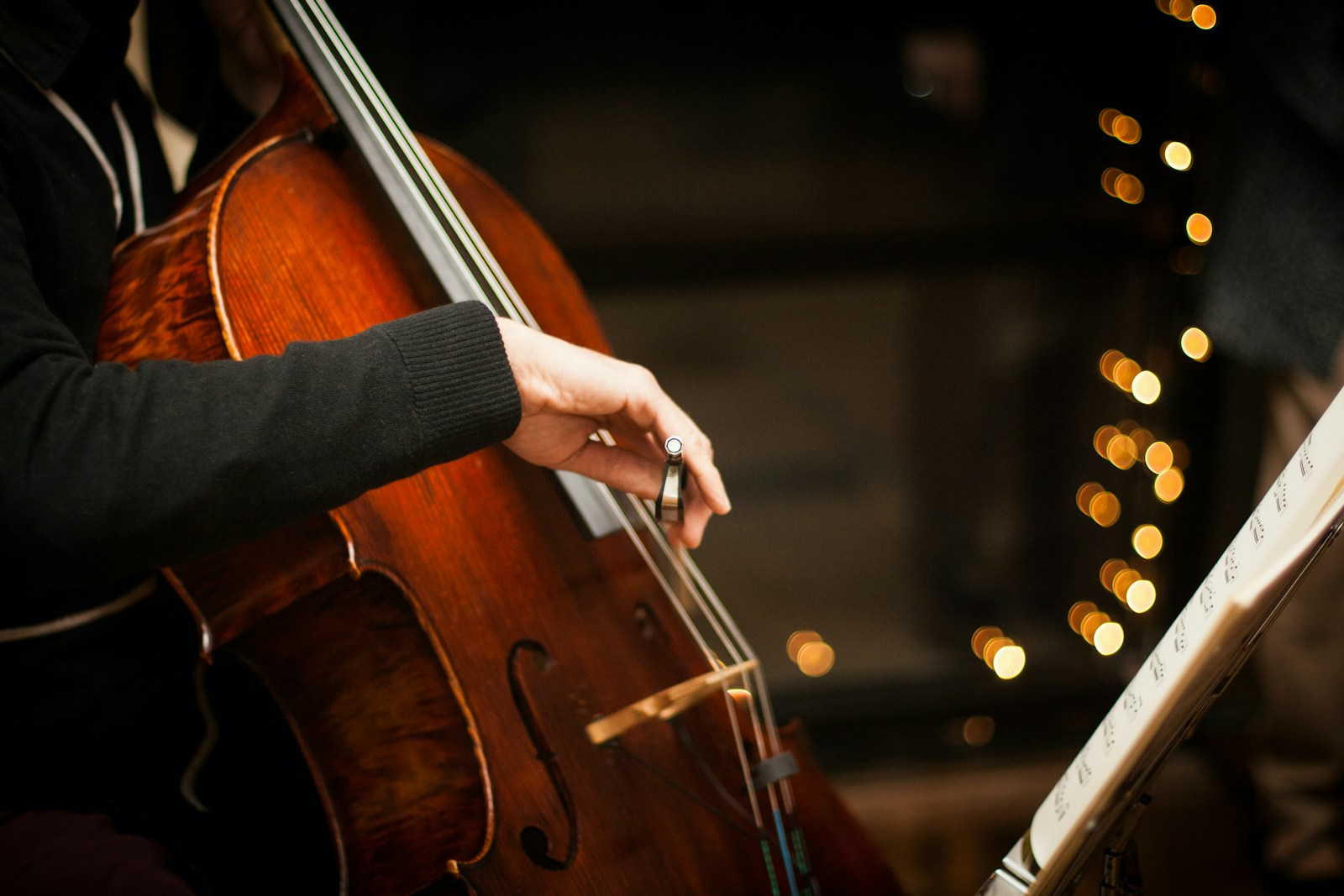 A cellist's bowing arm mid-stroke, warm lights behind