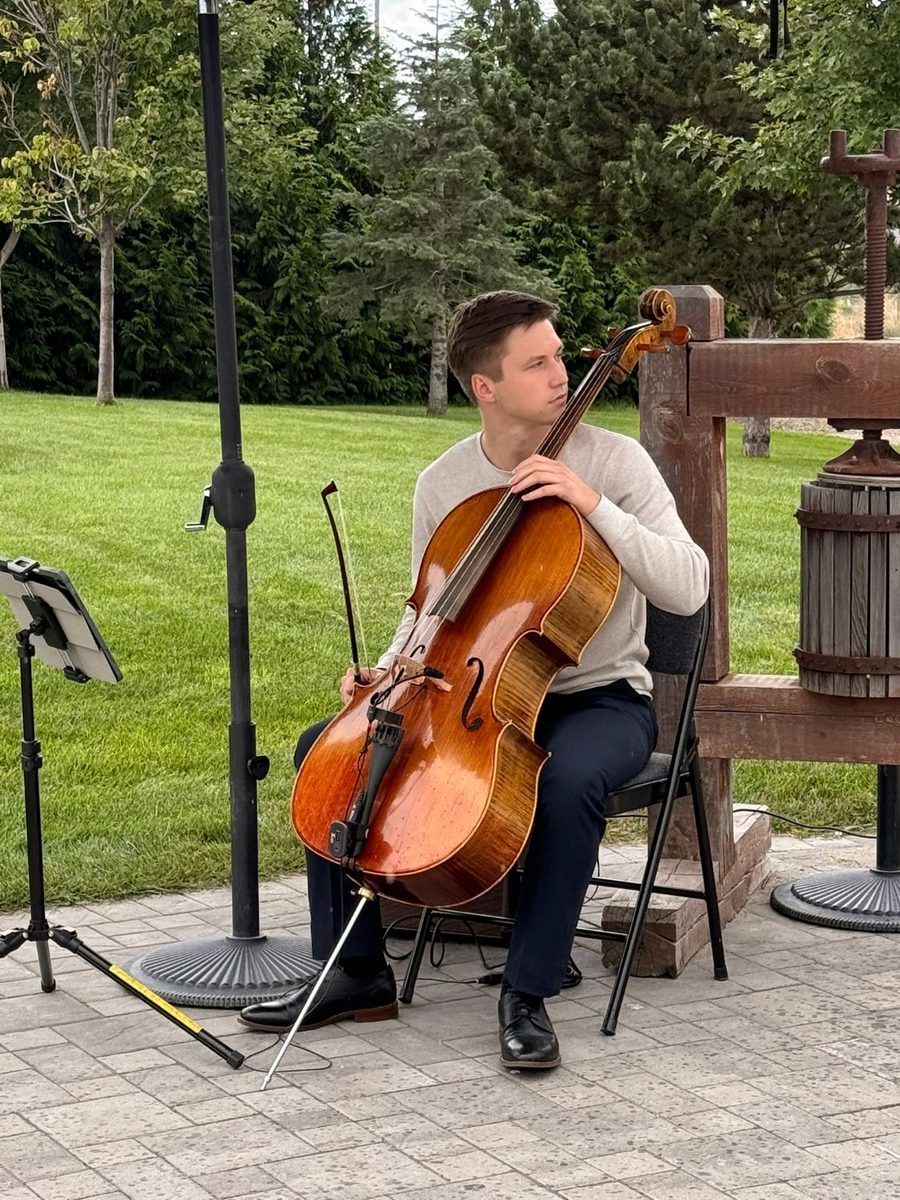 Yaroslav sitting with his cello on a lawn at an outdoor wedding
